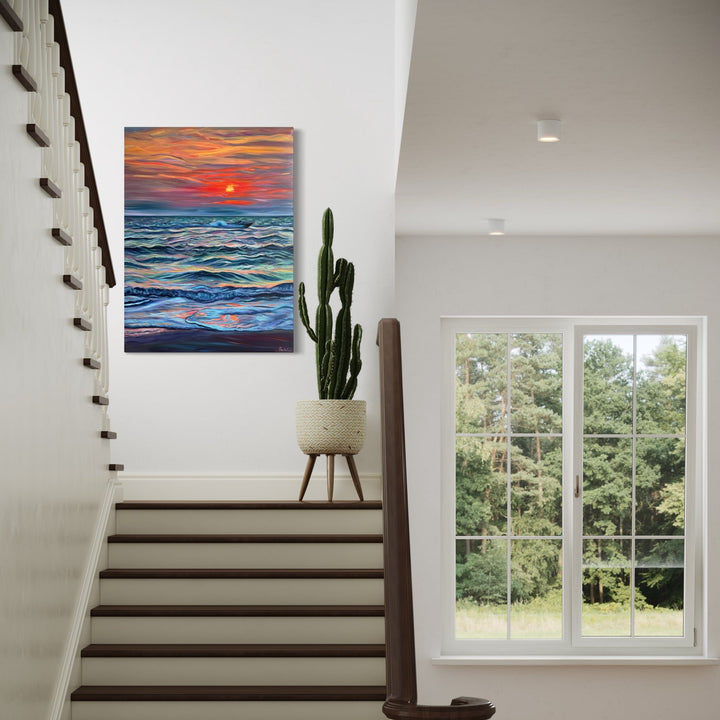 The artwork 'The Moment Is All There Is' by Claudia Robles-Gil features a vibrant seascape at sunset, with dynamic brushstrokes depicting rolling ocean waves in shades of deep blue and turquoise beneath a dramatic orange and red sky. A glowing sun hovers above the horizon, casting warm reflections on the textured waters created through bold oil and acrylic techniques.