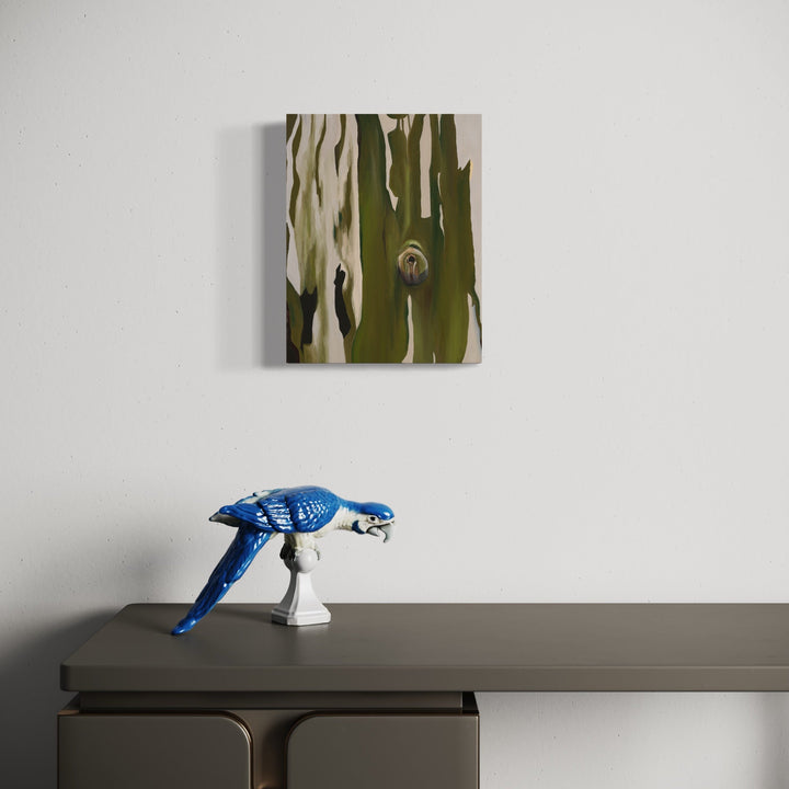 The artwork 'The Past is an Abyss, The Future is an Abyss' by Taylor Stoneman features abstract vertical strokes in olive green and cream tones on linen canvas, displayed above a minimalist gray surface with a decorative bright blue bird figurine. Oil painting technique creates textural depth and organic flowing patterns, measuring 14x11 inches.