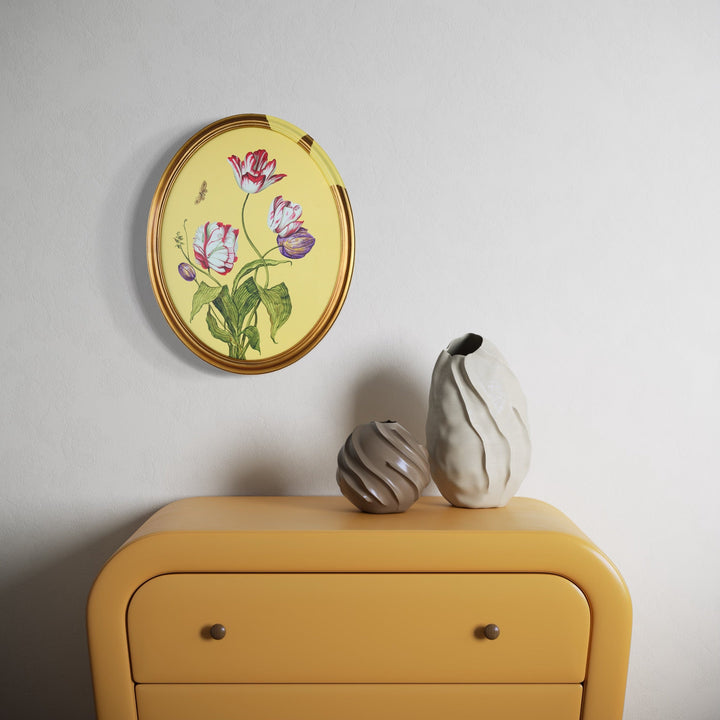 The artwork 'Tulips and Wings I' by Carlos Gamez de Francisco depicts delicate pink and purple tulips with green stems against a soft yellow background in an oval gold frame. The botanical illustration showcases graceful brushstrokes and realistic details in acrylic on canvas, measuring 16x20 inches. The piece hangs above a mustard-colored dresser with decorative ceramic vases.