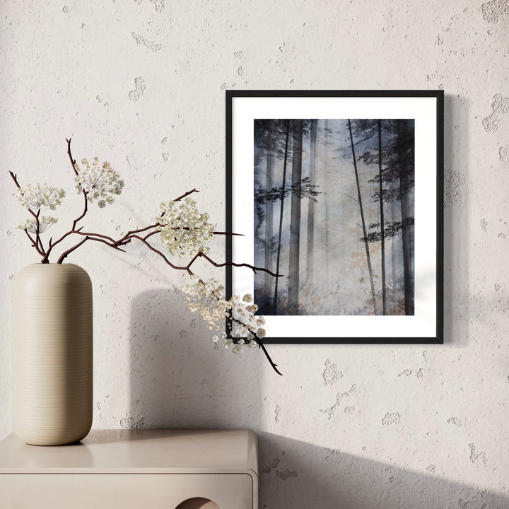 The artwork 'Whispers of the Canopy' depicts a misty forest scene in watercolor, featuring tall, ethereal pine trees silhouetted against a soft, foggy background. The monochromatic palette in shades of grey creates a mysterious, atmospheric mood. The black frame and white matting enhance the dramatic contrast. By Cat Lencke.