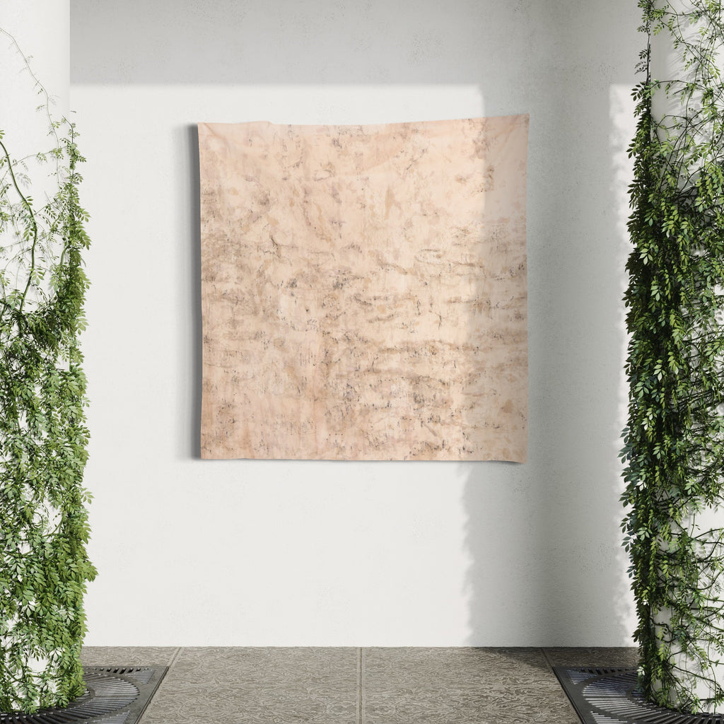 Distorsione di muro X by Jacqueline Ferrante features a large square abstract composition showcasing textural variations in muted peach and beige tones. Created with wine-soaked linen, coffee, natural dyes, and charcoal, the piece displays organic mottled patterns and subtle distressed effects against a white wall, framed by cascading green foliage.