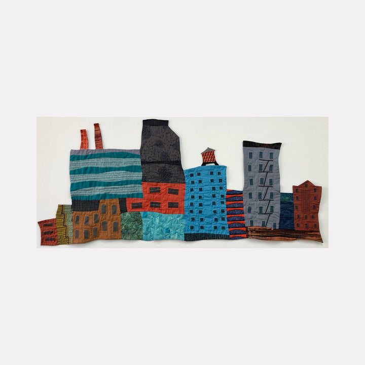 Cityscape with Smokestacks and Water Tower by Ann Cofta features a handcrafted fabric art depicting an urban industrial skyline. Vibrant turquoise, orange, and blue buildings with textured details are arranged against a white background. The mixed-media piece combines quilting and applique techniques, showcasing factory smokestacks and architectural elements in a contemporary folk art style by Ann Cofta.