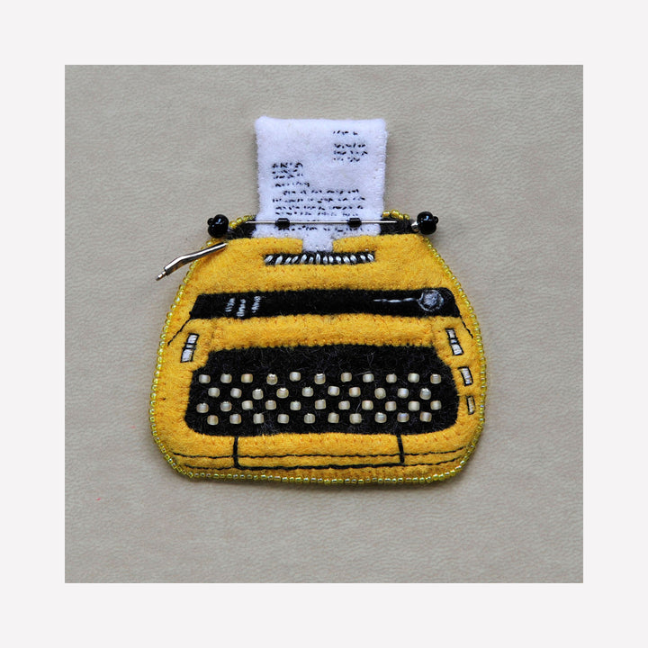 Vintage Typewriter (Smith Corona Sterling) by Ann Cofta: Hand-embroidered felt artwork depicting a bright yellow typewriter with black keys and white paper, featuring intricate beadwork details and wire accents. The miniature piece showcases meticulous craftsmanship with textured wool felt and dimensional elements.