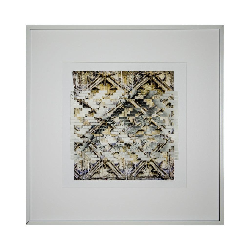 The artwork 'Indirection' by Kiana Honarmand features an intricate geometric pattern of hand-cut and woven giclee prints. The composition displays overlapping diagonal lines creating X-shaped motifs in muted gold, beige, and gray tones. The textural layering effect produces a complex, abstract design with weathered, vintage-like qualities, framed in crisp white matting and a minimalist silver frame.