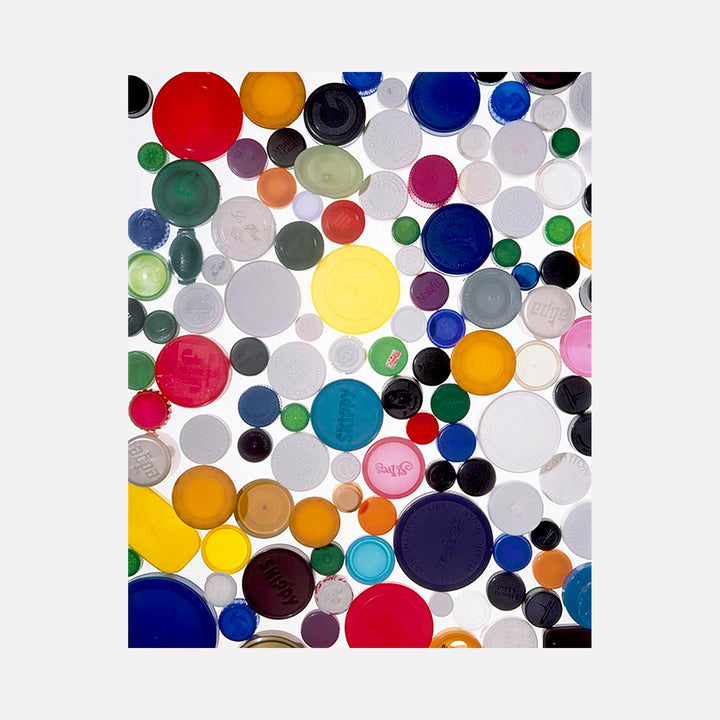 The artwork 'MDC' by Dirk Westphal features vibrant circular plastic bottle caps arranged in a dynamic pattern. Multicolored caps in red, blue, yellow, green, and white create an abstract composition against a light background. Various sizes of caps create depth and visual rhythm in this 24x20 inch signed photographic print.