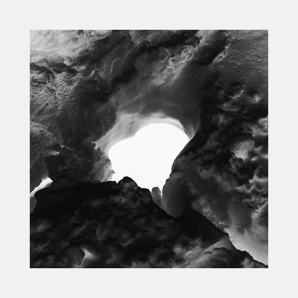 The artwork 'Tunnel of Snow' by Cavier Coleman captures a dramatic black and white photograph of a natural snow formation creating a tunnel-like aperture. The stark contrast between the bright opening and dark, textured snow walls creates an ethereal cave-like perspective. The crystalline texture of packed snow forms intricate patterns along the tunnel's edges, photographed in 24x24 inches by Cavier Coleman.