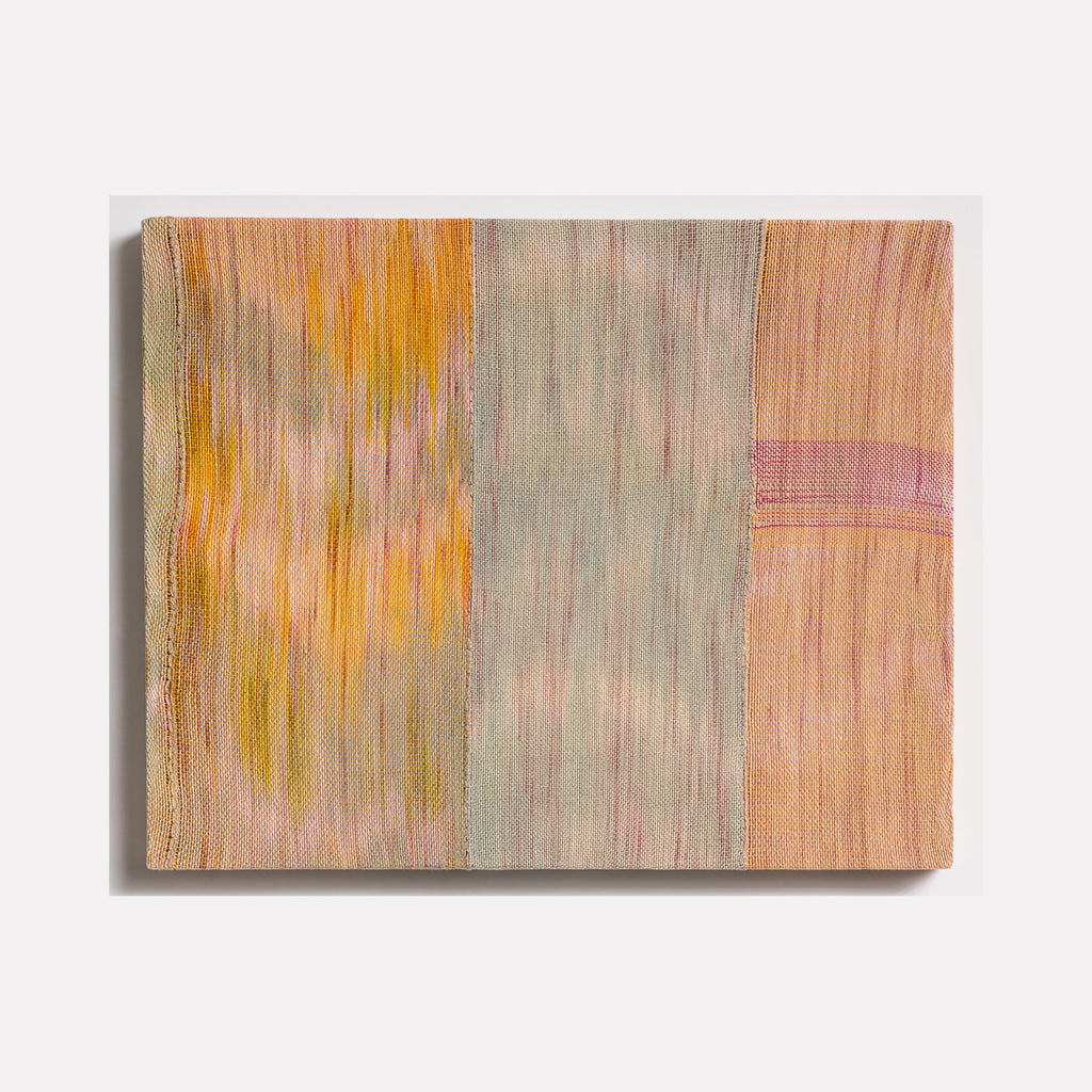 The artwork 'Untitled 107' by Victoria Manganiello features vertical panels of woven fibers in muted peach, sage gray, and golden yellow tones. Abstract brushstroke-like patterns create a gentle vertical movement across the textile surface, with subtle color transitions and textural elements achieved through natural and synthetic fiber blending. 24x32 inches.