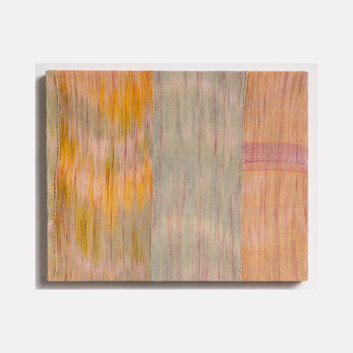 The artwork 'Untitled 107' by Victoria Manganiello features vertical panels of woven fibers in muted peach, sage gray, and golden yellow tones. Abstract brushstroke-like patterns create a gentle vertical movement across the textile surface, with subtle color transitions and textural elements achieved through natural and synthetic fiber blending. 24x32 inches.
