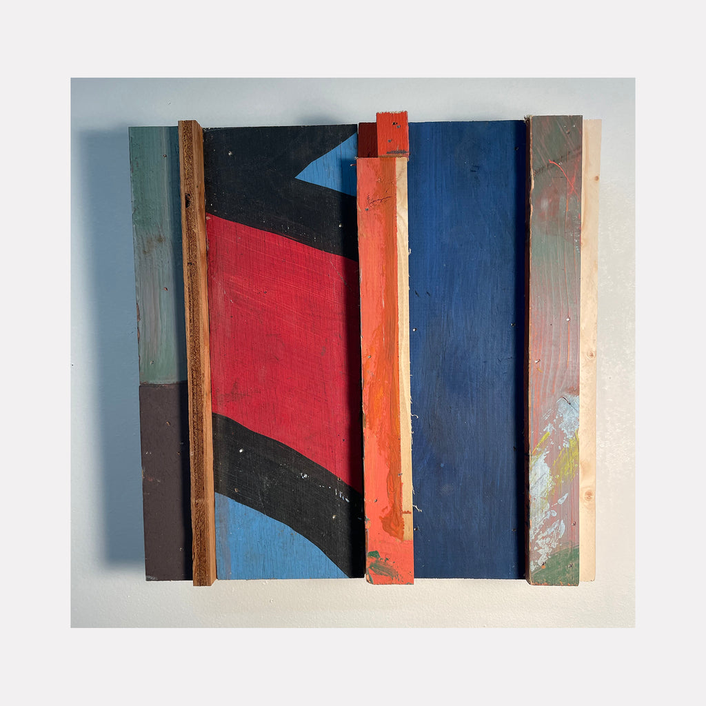 The artwork 'Verify In Field' by Simon Draper features a geometric abstract composition of painted wood assemblage. Vertical wooden planks in vibrant red, navy blue, and black create a dynamic composition with angular shapes. The textured wood surface and bold color blocks form a modernist architectural aesthetic within the 12x12 inch frame. By Simon Draper.