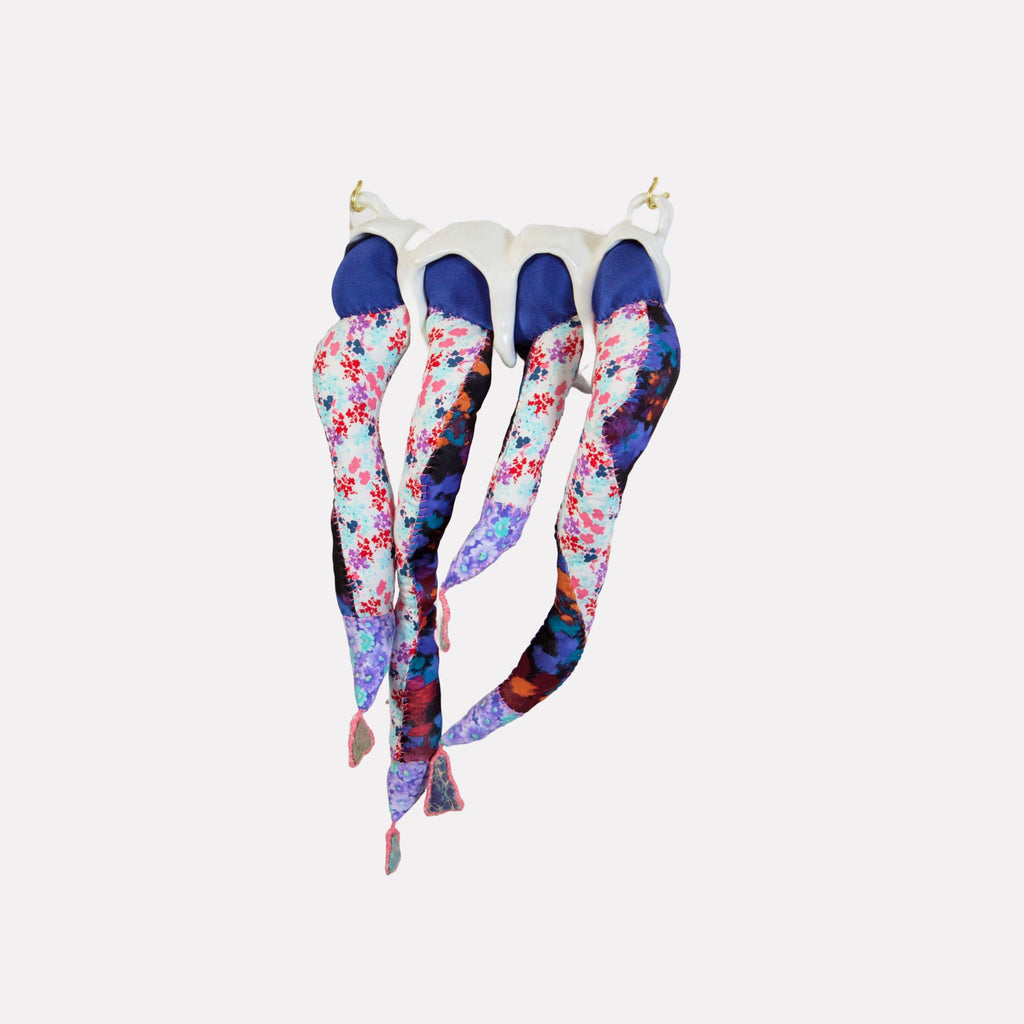 Four Chambers by Hanna Washburn is a delicate textile sculpture featuring elongated, tubular forms in vibrant floral patterns and deep indigo tones, suspended from a soft white base. The piece blends intricate fabric layering with organic, flowing shapes to create a dynamic, evocative art object with a graceful presence.