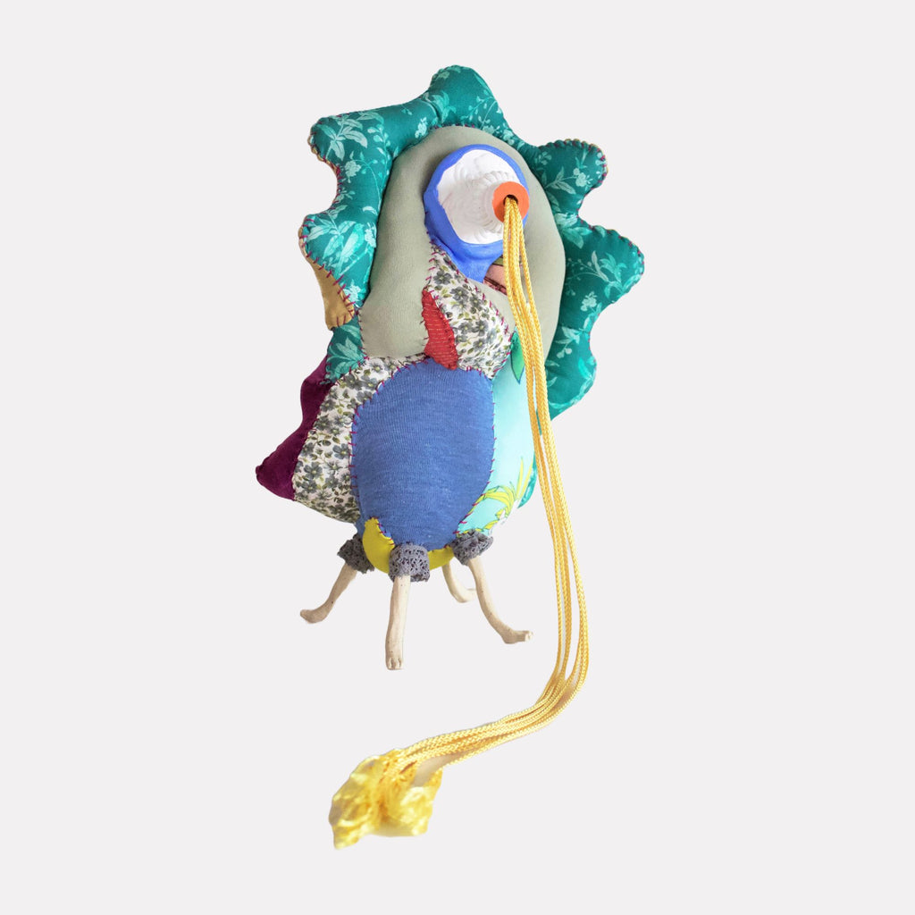 Nectary by Hanna Washburn is a whimsical textile sculpture resembling a stylized bird with layered fabrics in vibrant blues, greens, and floral patterns. Detailed stitching and a trailing yellow cord add tactile complexity, blending organic shapes with playful craftsmanship in a unique, imaginative form.