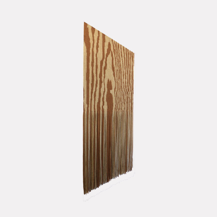 The artwork "Slant Fringe" by Quynn Douglas Dale features a vertical rectangular piece with a wood grain pattern in warm brown and beige tones, transitioning into long, narrow fringes that hang downward. The design evokes minimalism and organic textures similar to works by Agnes Martin and Eva Hesse, blending natural motifs with abstract repetition.