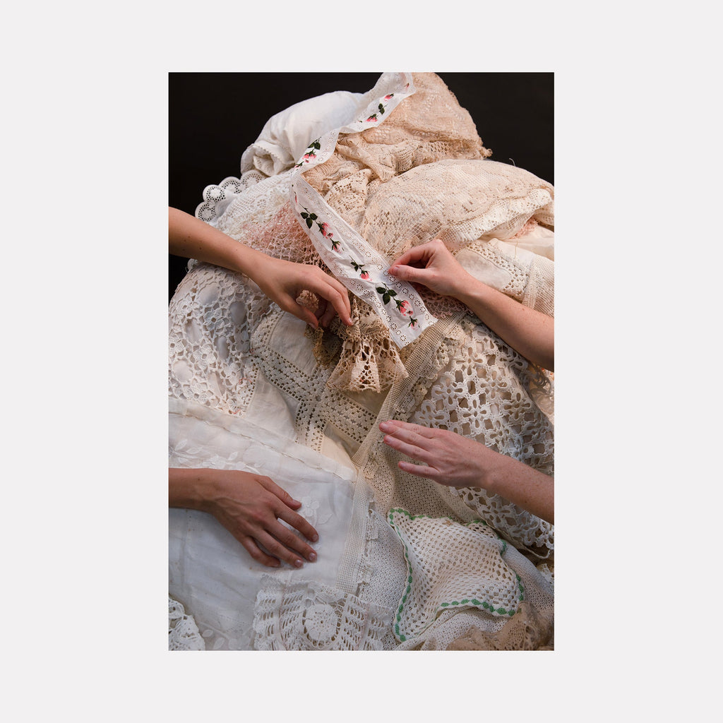 The artwork "080A8277" by Eunice Pais captures hands working with layered textiles featuring intricate crochet, lace, and embroidered fabric in warm cream and beige tones. The tactile surfaces and intimate composition evoke the delicate craft of Magdalena Abakanowicz’s fiber sculptures and the contemplative portraiture of Nan Goldin.