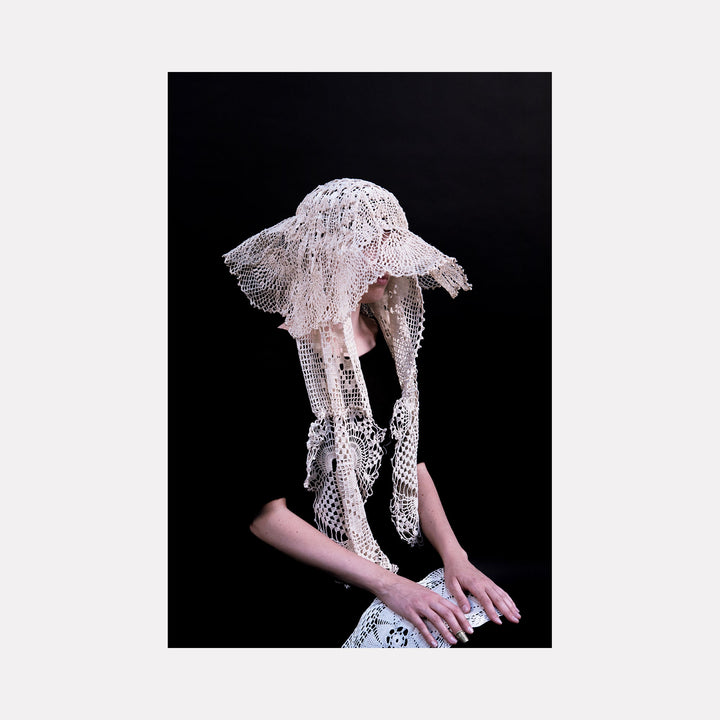 The artwork "080A86891" by Eunice Pais features a delicate, lace-like headpiece and gloves in soft beige tones against a deep black background. The intricate crochet patterns and elongated forms evoke the detailed craftsmanship reminiscent of Louise Bourgeois’s textile sculptures and the ethereal quality found in Eva Hesse’s mixed media works.
