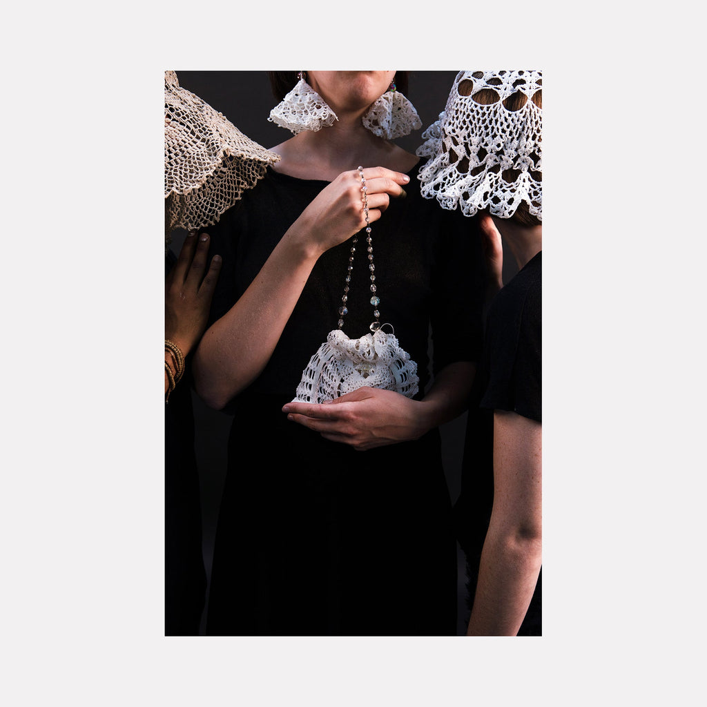 The artwork "080A8824" by Eunice Pais features a close-up of three figures clad in black, adorned with intricate white crocheted accessories and lace framing their faces and shoulders. The delicate textures and craftsmanship evoke the tactile elegance of Louise Bourgeois’s fabric sculptures and the intimate portraiture style of Nan Goldin.
