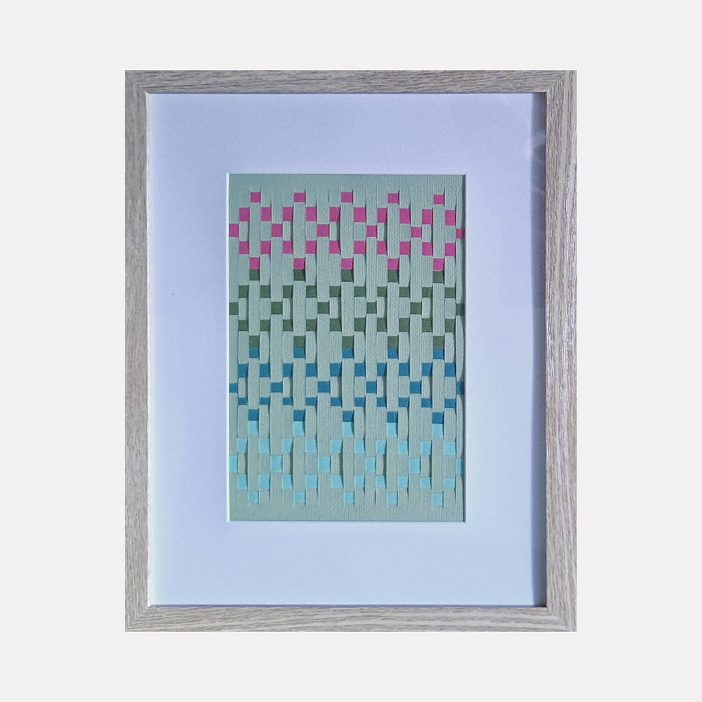 The artwork "Diamond Weave" features a textured geometric pattern of interlacing rectangles in shades of pink, green, blue, and white, creating a gradient effect on a light mint green background. The piece is framed in a simple light wood frame with a white mat. Diamond Weave by Johanna Ryan.
