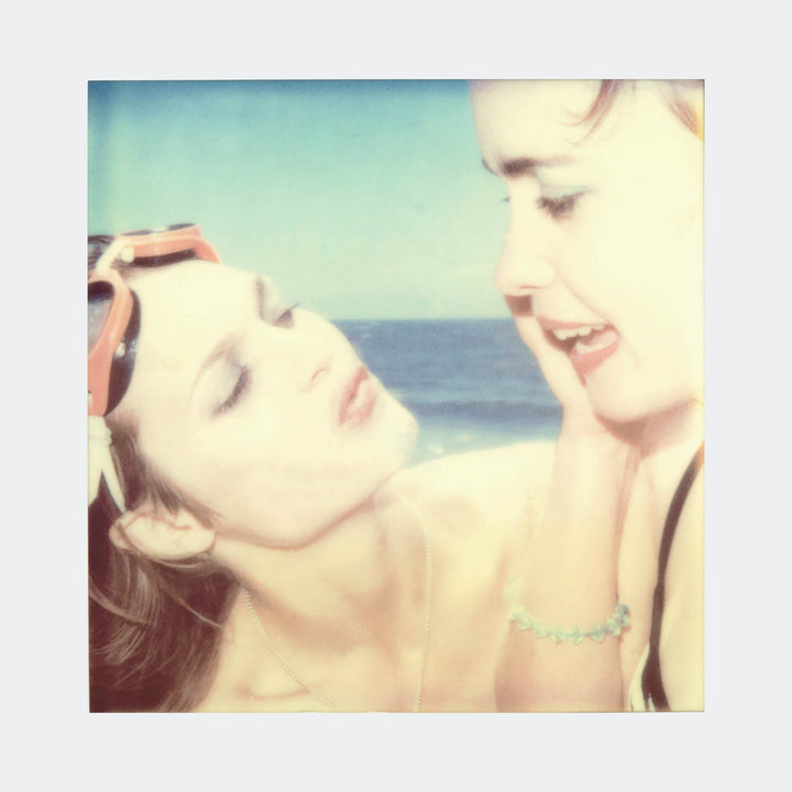 The artwork "Untitled (Beachshoot) 1400" by Stefanie Schneider captures a dreamy, vintage-style beach moment with soft focus and muted pastel tones. The composition features two women in close interaction, evoking the nostalgic and intimate atmosphere reminiscent of Polaroid photography and the emotive style of Nan Goldin’s portraits.