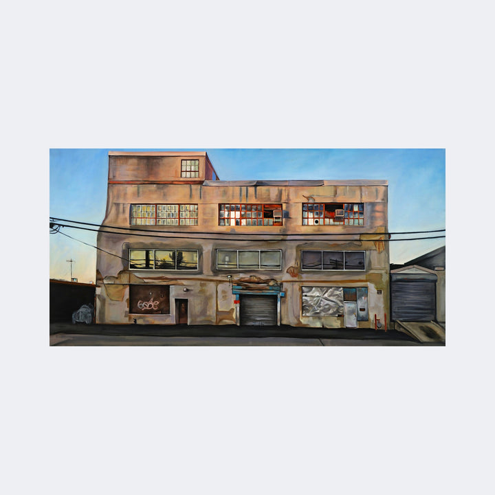 The artwork "Urban Monoploy, NY Avenue" by Regina Miele depicts a weathered industrial building with textured walls in muted earth tones under a clear blue sky. The detailed portrayal of windows, doors, and electrical wires evokes a gritty urban realism reminiscent of Edward Hopper’s architectural scenes and the precise style of Richard Estes.