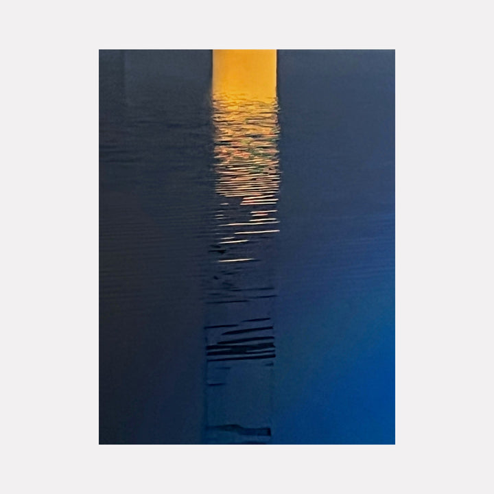The artwork "Amarillo Melt" features a vertical rectangular yellow shape reflected on a rippled dark blue water surface, blending hues of blue and hints of orange in a serene, abstract style with smooth texture and subtle color gradients. The piece evokes calm with minimalist composition by Starr Tucker-Ortega.
