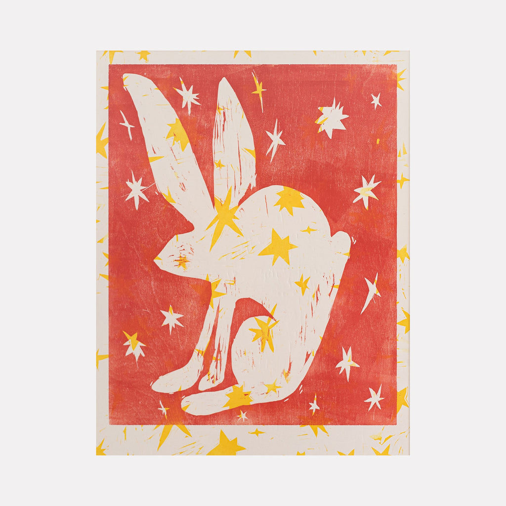 The artwork "Apparition" features a white silhouette of a crouching rabbit with elongated ears, set against a textured warm red background. The rabbit and surrounding space are adorned with scattered yellow star shapes, creating a mystical and whimsical atmosphere. The piece blends simple forms with vibrant contrasting colors in a modern style. By Ashley Ranae Quick.