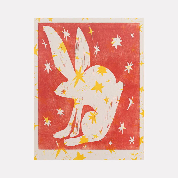 The artwork "Apparition" features a white silhouette of a crouching rabbit with elongated ears, set against a textured warm red background. The rabbit and surrounding space are adorned with scattered yellow star shapes, creating a mystical and whimsical atmosphere. The piece blends simple forms with vibrant contrasting colors in a modern style. By Ashley Ranae Quick.