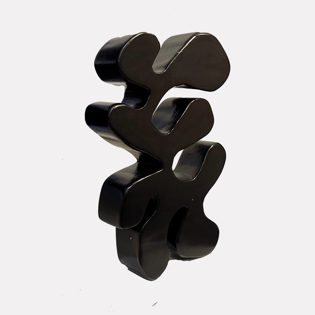 Be still and know that you are god features a smooth, abstract black sculpture with organic, rounded forms stacked vertically, creating a modern minimalist shape that evokes calm and thoughtful energy, designed by Shadia Sabagh.