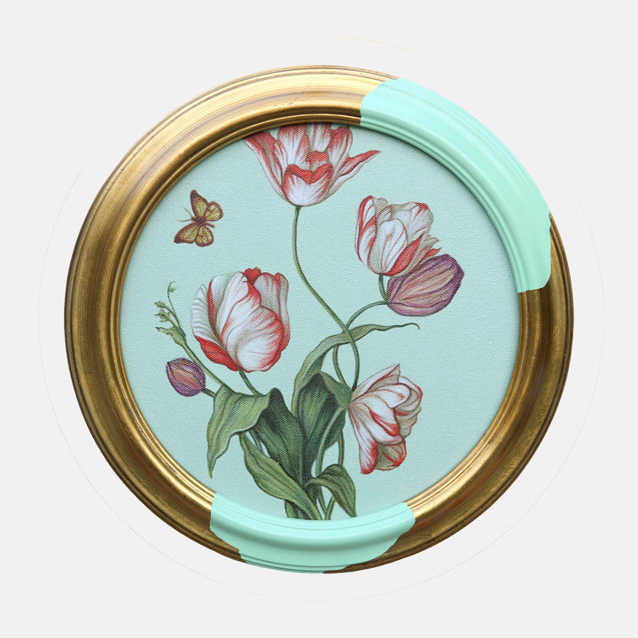 The artwork "Six Tulips and a Butterfly" by Carlos Gamez de Francisco features a delicate botanical composition of six tulips in soft pinks, reds, and purples, with detailed green leaves and a small butterfly against a pale blue background. The round frame blends classic gold with modern pastel accents, evoking the refined naturalism of Maria Sibylla Merian and the elegant floral studies of Pierre-Joseph RedoutÃ©.