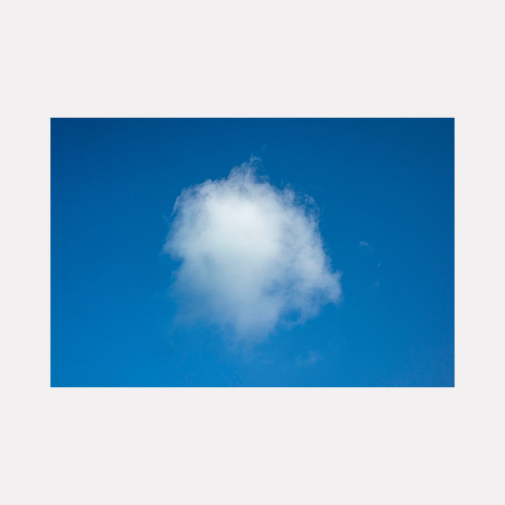 Clouds by Steve Edson depicts a single, soft white cloud floating against a vivid, deep blue sky, highlighting the simplicity and calm beauty of a clear day with delicate, wispy edges that suggest gentle movement and tranquility.