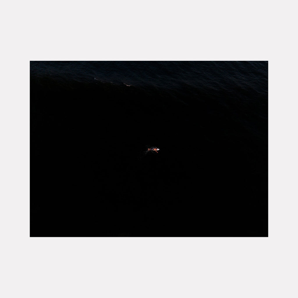 The artwork "Where I Begin Again" by Dennis Maida features a solitary figure floating on dark, textured waters, evoking themes of isolation and renewal. The deep black and subtle blue tones resemble minimalist and contemplative styles found in works by Mark Rothko, highlighting contrast and emotional depth. Dennis Maida.