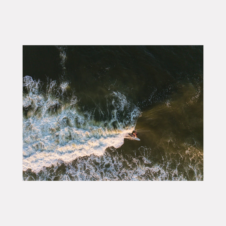 The artwork "Rip It" by Dennis Maida features an aerial view of a surfer riding a wave in dark, textured ocean waters. The composition highlights dynamic movement with frothy white wave patterns contrasting against deep green and brown hues, reminiscent of impressionist water studies by artists like Claude Monet. Dennis Maida.