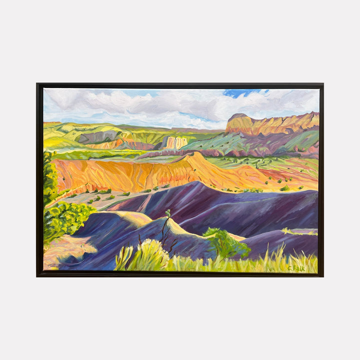 The artwork "Dreamland" by Connie Falk features a vibrant landscape with rolling hills and mesas in rich hues of orange, purple, and green, reminiscent of the bold color palettes and fluid forms found in the works of Georgia O'Keeffe. The textured brushstrokes and dynamic composition evoke a serene yet dramatic natural scene bathed in sunlight under a partly cloudy sky.