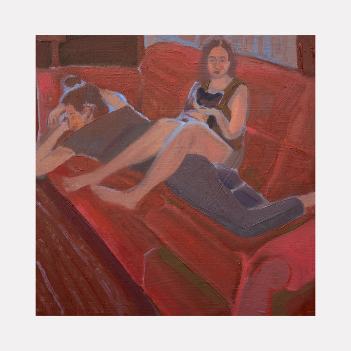 The artwork "God gave us pleasure [roommates and our cat]" depicts two figures lounging on a red sofa, one resting face down while the other sits holding a small black cat. The painting uses warm, muted tones with soft brushstrokes emphasizing a relaxed, intimate domestic scene. By Chelsie Sunde.