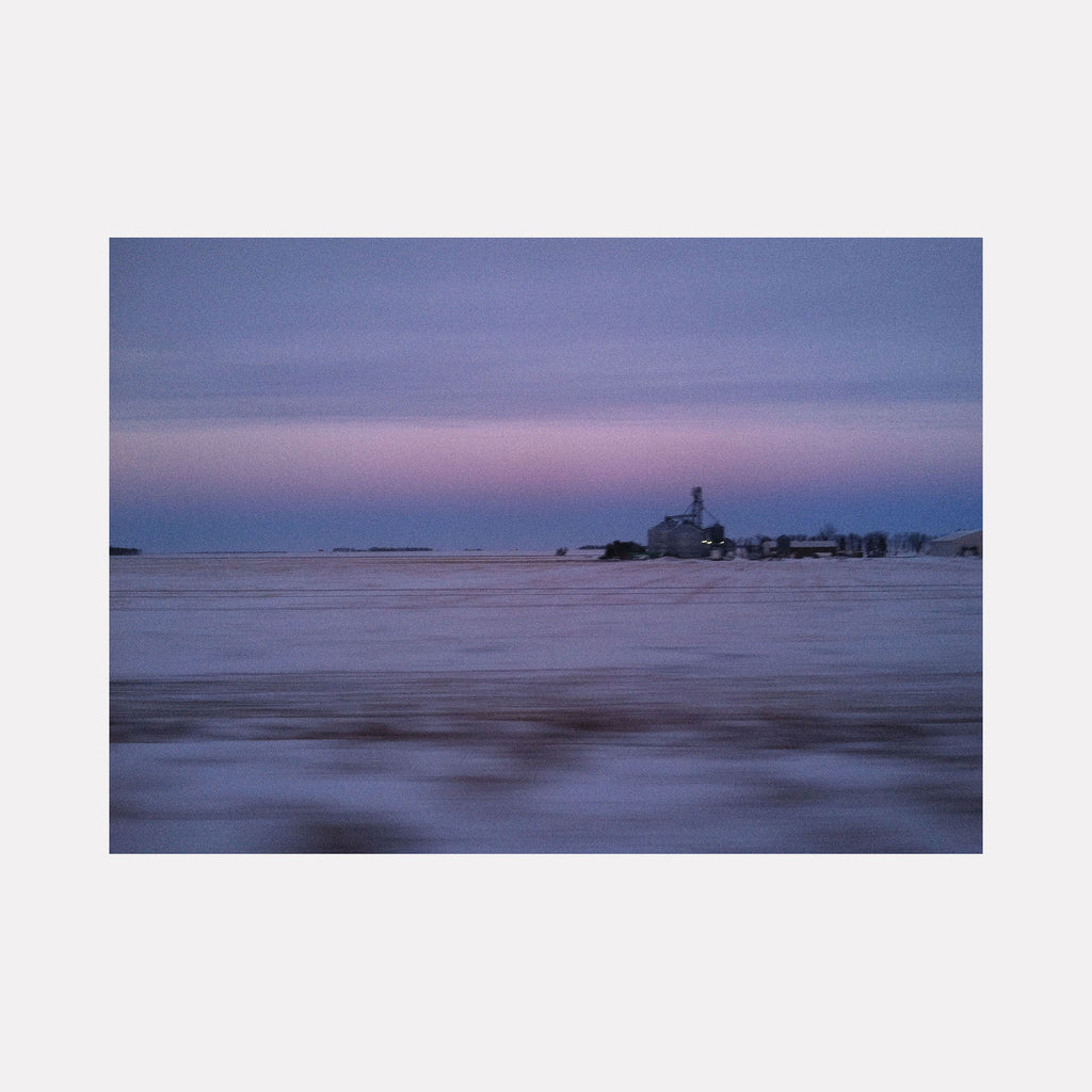 The artwork "Good Morning Indiana" by Kelly McGovern captures a serene rural landscape at dawn, featuring a soft, muted palette of blues, purples, and pinks that blend gently across a snowy field. The distant farmhouse and silos evoke a sense of quiet isolation, reminiscent of the atmospheric tones found in Andrew Wyeth’s realist paintings, with a subtle impressionistic softness in texture.