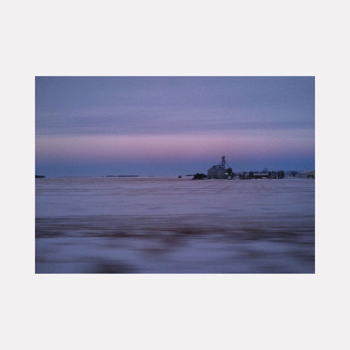 The artwork "Good Morning Indiana" by Kelly McGovern captures a serene rural landscape at dawn, featuring a soft, muted palette of blues, purples, and pinks that blend gently across a snowy field. The distant farmhouse and silos evoke a sense of quiet isolation, reminiscent of the atmospheric tones found in Andrew Wyeth’s realist paintings, with a subtle impressionistic softness in texture.