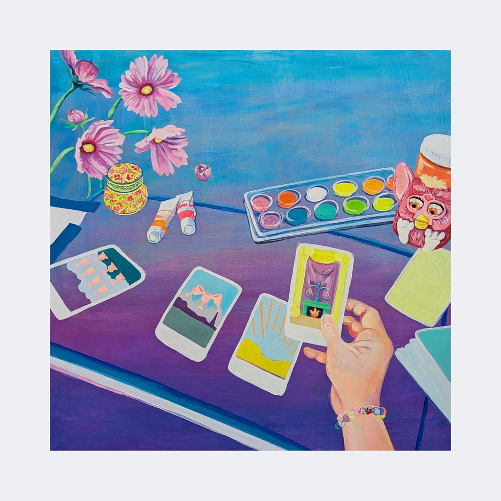 The artwork "Justice in Her Hands" by Mary Younkin features a vibrant acrylic painting on a wood panel with a 30 by 30 inch dimension. It depicts a hand holding a colorful tarot card above a purple table scattered with tarot cards, a watercolor paint set, pink flowers in a vase, paint tubes, and a whimsical owl container, evoking styles reminiscent of Mary Blair's playful color palette and flat illustrative shapes.