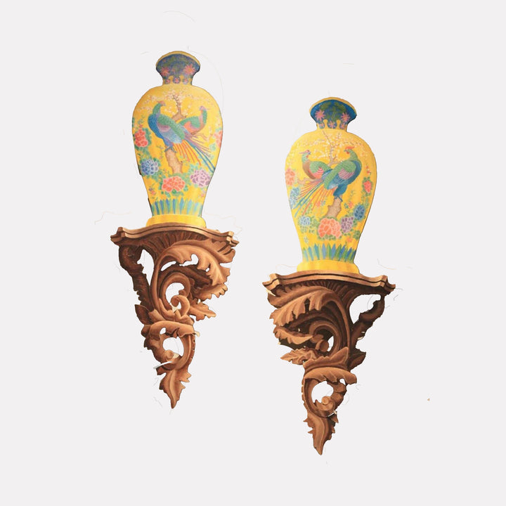 The artwork "Kutani Birds" by Carl Chaiet in gallery position 1 showcases a pair of elegant yellow porcelain vases adorned with vibrant illustrations of green and red birds amidst colorful blossoms. Each vase is perched on an ornately carved wooden bracket with swirling, leafy motifs, evoking the refined craftsmanship and natural themes reminiscent of Alphonse Mucha and Charles Rennie Mackintosh.
