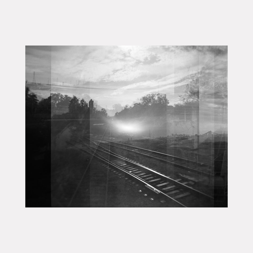 The artwork "Light of The Well" by Kelly McGovern features a monochromatic, layered composition of railway tracks vanishing into a glowing light source in the distance, blending natural elements like trees with abstract overlays. Its style echoes the surreal, dreamlike qualities of Man Ray and the contemplative urban scenes reminiscent of Edward Hopper.