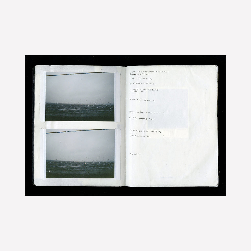 The artwork "Lost Car" by Kelly McGovern features an open sketchbook with two muted seascape photographs showcasing a calm ocean under a gray sky. The right page contains faint handwritten notes in a minimalist, conceptual style reminiscent of Robert Frank’s documentary photography and the quiet introspection found in works by Nan Goldin.