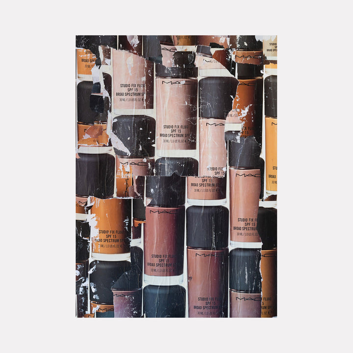 The artwork "MAC Wall" features a textured collage of various MAC Studio Fix Fluid foundation bottles arranged closely together. The image highlights different skin-tone shades in beige, tan, deep brown, and black caps with visible wear and peeling effects, creating an abstract, urban aesthetic. Product by Amy Turner.