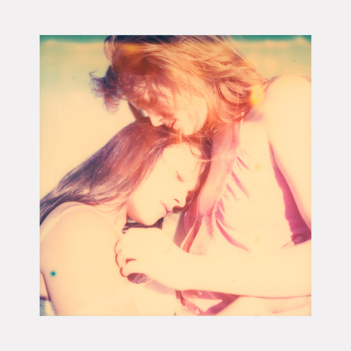 The artwork "Making Out in Car (Till Death do us Part)" showcases a tender moment between two women bathed in soft, warm light with a vintage, dreamy texture and faded pastel colors, emphasizing intimacy and affection. The image features subtle grain and a nostalgic style, by Stefanie Schneider.