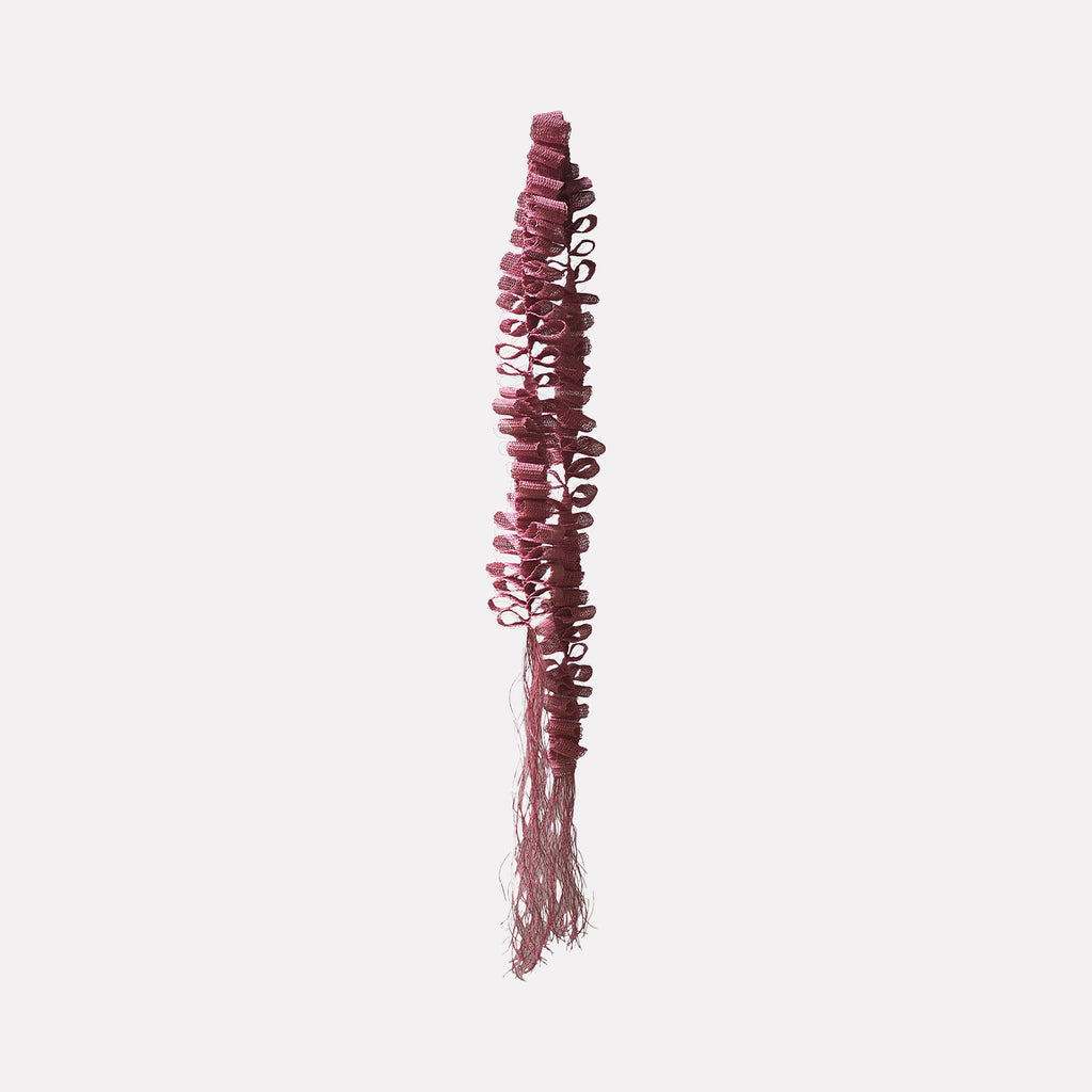 The artwork "Desire Paths" by Morgan Hale features a vertical, textured sculpture composed of intricate, looped pink fibers that cascade down into delicate fringe. Its organic form and playful structure echo the tactile qualities of Louise Bourgeois’s soft sculptures and the minimal, repetitive patterns reminiscent of Eva Hesse’s fiber works.