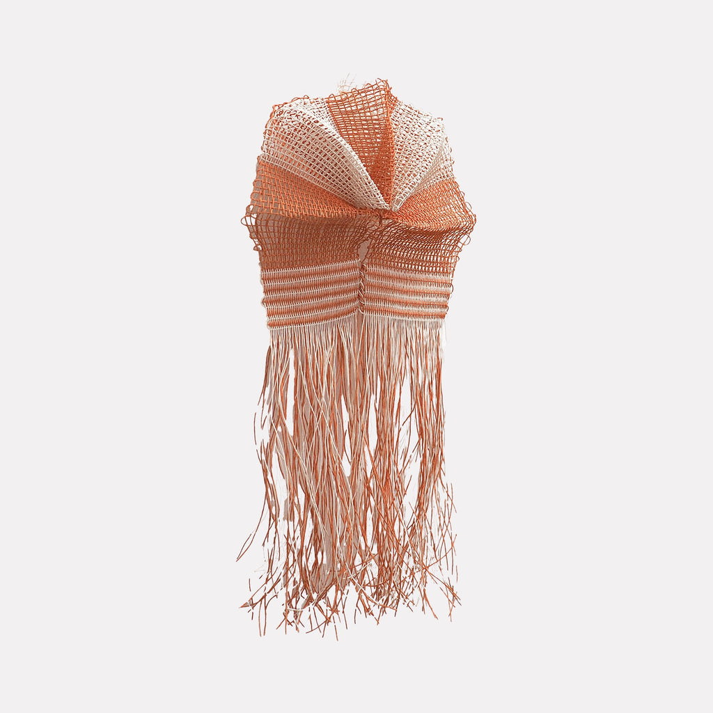 The artwork "Red Cloud" by Morgan Hale features a textured, woven sculpture in warm red and cream tones, combining mesh-like fabric and striped patterns. Long, flowing fringe elements hang from the bottom, evoking a sense of movement reminiscent of fiber art by Sheila Hicks and the abstract forms of Eva Hesse.