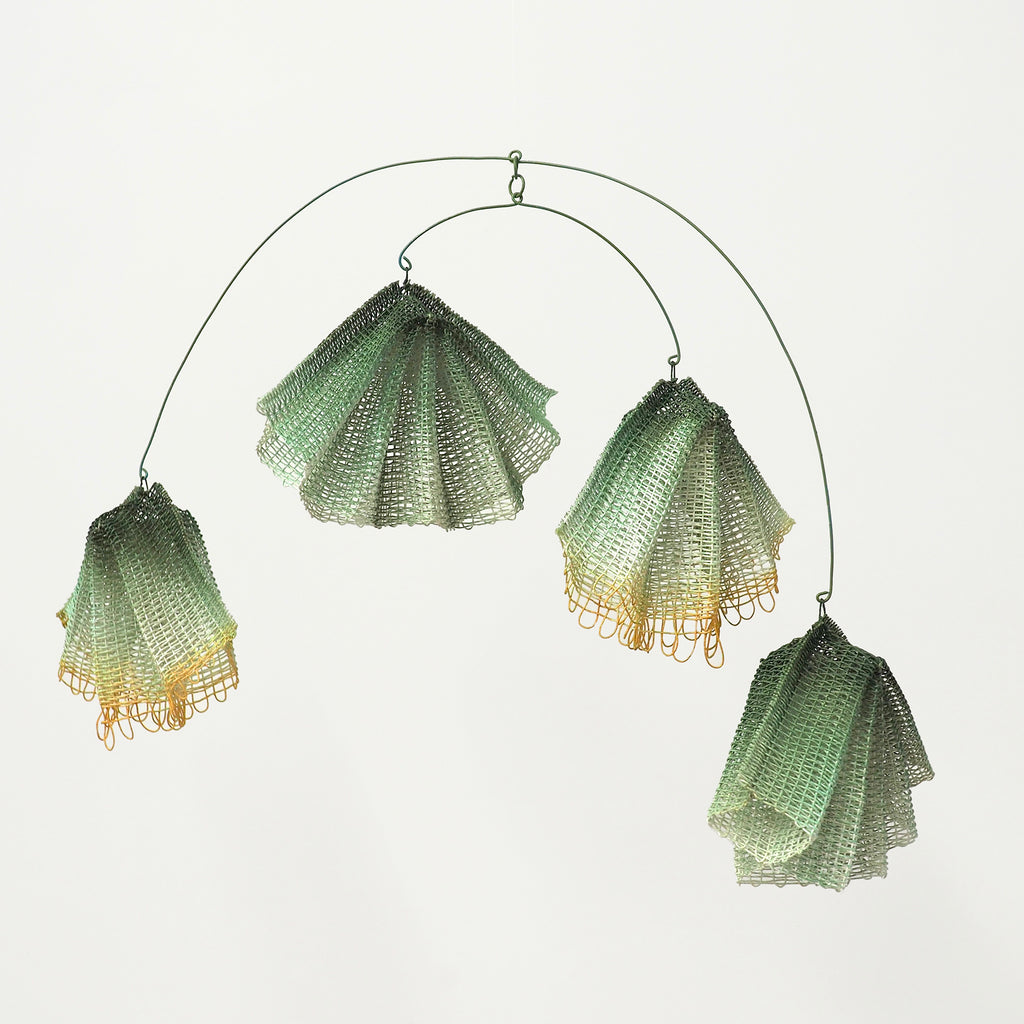 The artwork "Solana" by Morgan Hale features delicate, translucent sculptural forms resembling seashells or blooming flowers, crafted from fine mesh material in gradient shades of green and soft yellow. The mobile structure and organic shapes evoke the fluidity and balance seen in Alexander Calder's kinetic sculptures, blending modern minimalism with natural elegance.