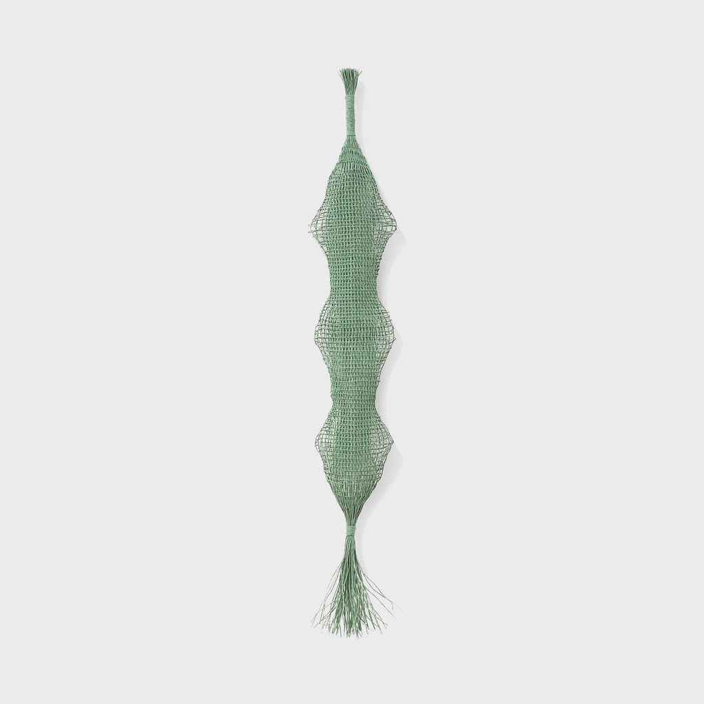 The artwork Verdant Pendant by Morgan Hale features an elongated, intricately woven green textile with a delicate mesh pattern and organic, undulating shapes reminiscent of natural forms. Its minimalist, textured design evokes influences from mid-century modern artists and the tactile qualities seen in Anni Albers' woven art.