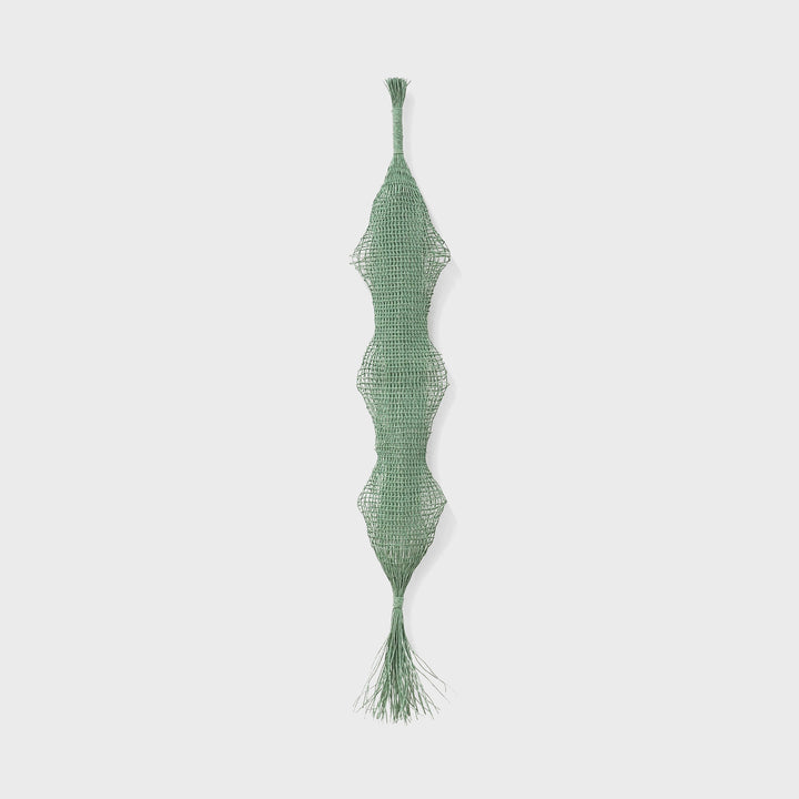 The artwork Verdant Pendant by Morgan Hale features an elongated, intricately woven green textile with a delicate mesh pattern and organic, undulating shapes reminiscent of natural forms. Its minimalist, textured design evokes influences from mid-century modern artists and the tactile qualities seen in Anni Albers' woven art.