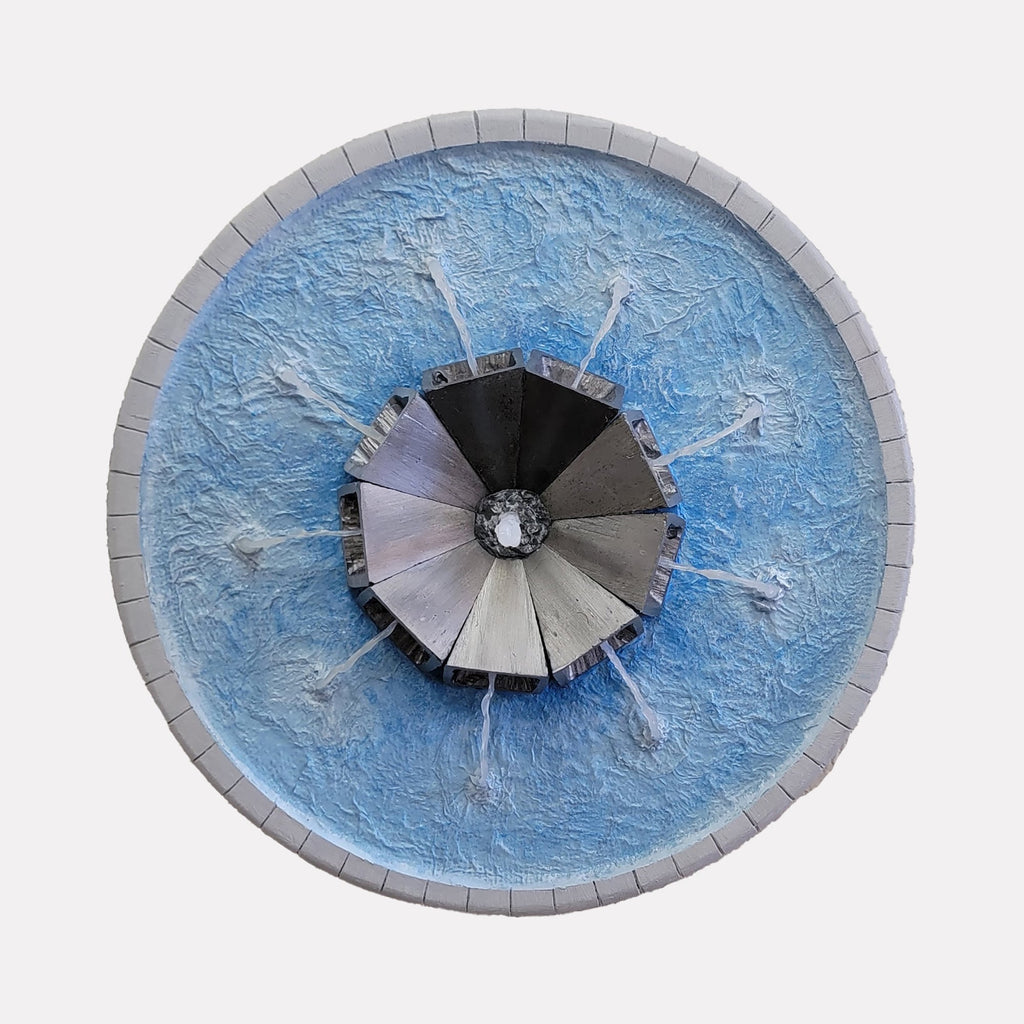 The artwork "Fountain Blue" by Richard Alpert features a circular design with a textured blue background resembling water. At its center is a metallic, segmented structure radiating outward with dynamic water jets, evoking a modernist aesthetic similar to the geometric abstraction seen in works by Frank Stella and the fluidity found in Alexander Calder’s mobiles.