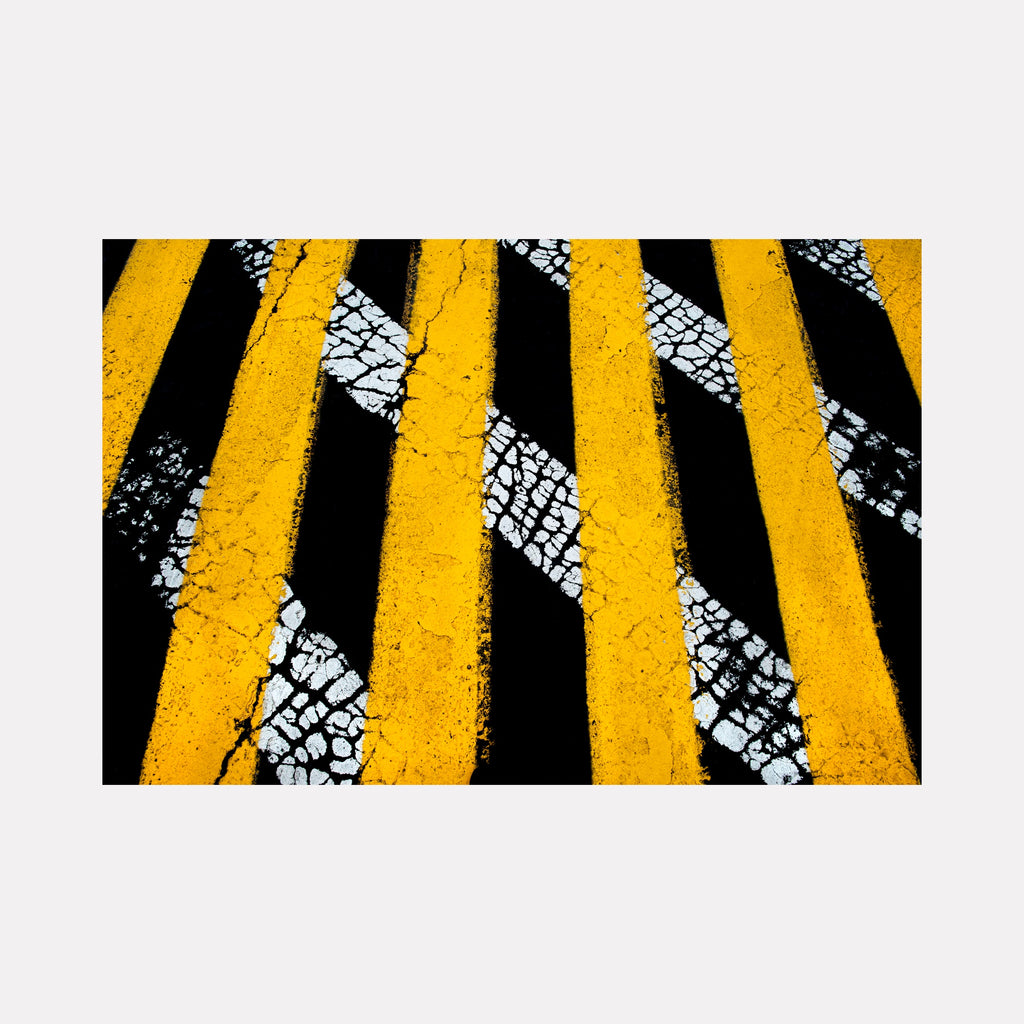 Road Paint 02 by Steve Edson presents a striking abstract pattern of bold yellow vertical stripes contrasted against a textured black background with irregular white cracked lines, creating a dynamic visual interplay between color, texture, and linear movement in a modern, urban-inspired composition.