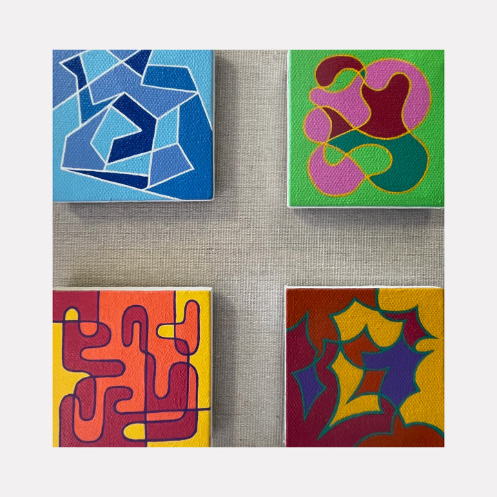 The artwork 'Seasonal Phenomena II' by Joe Piscopia features four vibrant abstract squares arranged in a grid pattern. Each square presents distinct geometric designs: a blue angular maze-like pattern, pink and green organic curves, orange and red interlocking pathways, and a purple-gold composition with flowing shapes. Painted in acrylic on canvas, each piece measures 13x13 inches.