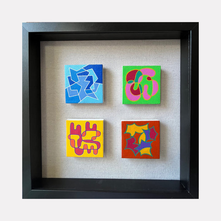 The artwork "Seasonal Phenomena I" by Joe Piscopia features four small square acrylic paintings on canvas, each with vibrant abstract shapes and bold colors including blue, green, yellow, red, and pink, arranged in a large black frame with a textured neutral background, showcasing dynamic compositions and intricate patterns.