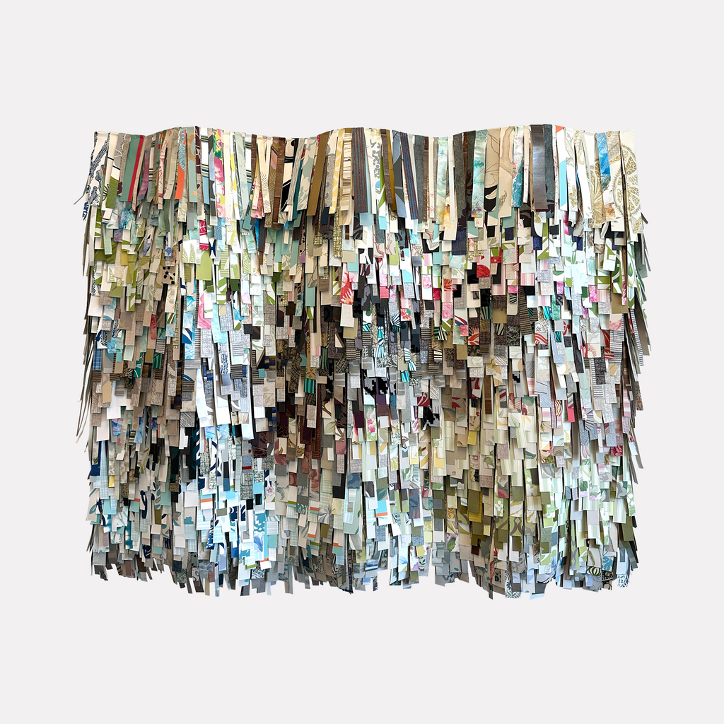 She's Got Curves by Shiri Phillips features an intricate layered composition of hanging, rectangular strips in a muted palette of blues, greens, creams, and soft earthy tones. The abstract artwork creates a textured, cascading effect with a rhythmic, tactile presence that invites close viewing and appreciation of its subtle color interplay.